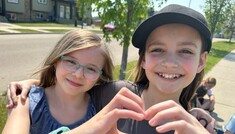 Two students standing side by side. Together their hands form a heart shape. They are smiling.