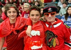 Three students all dressed in red wearing red plastic capes and red head bands. They are standing side by side with arms around each other, in the context of a school pep ralley.