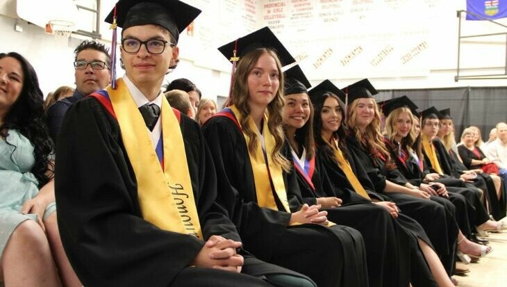 Graduates from Spruce View sit in a row, smiling at a speaker or presentation at their grad ceremony